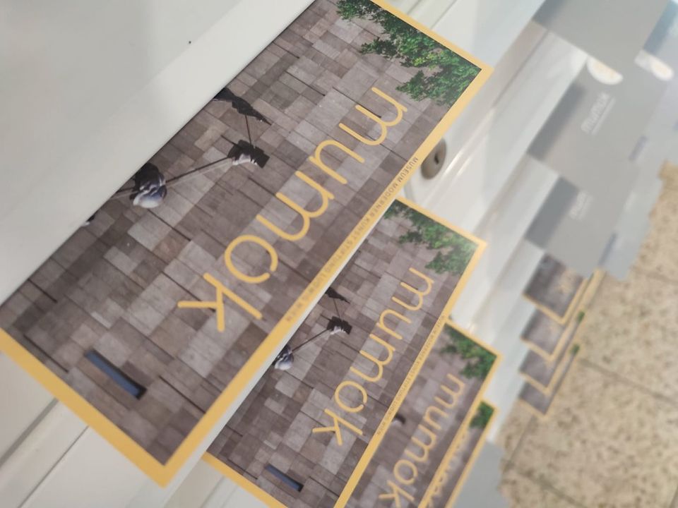 Mehrere "mumok"-Museumsbroschüren in einem Schaukasten mit einem Foto von Menschen, die auf grauen Steinfliesen laufen.